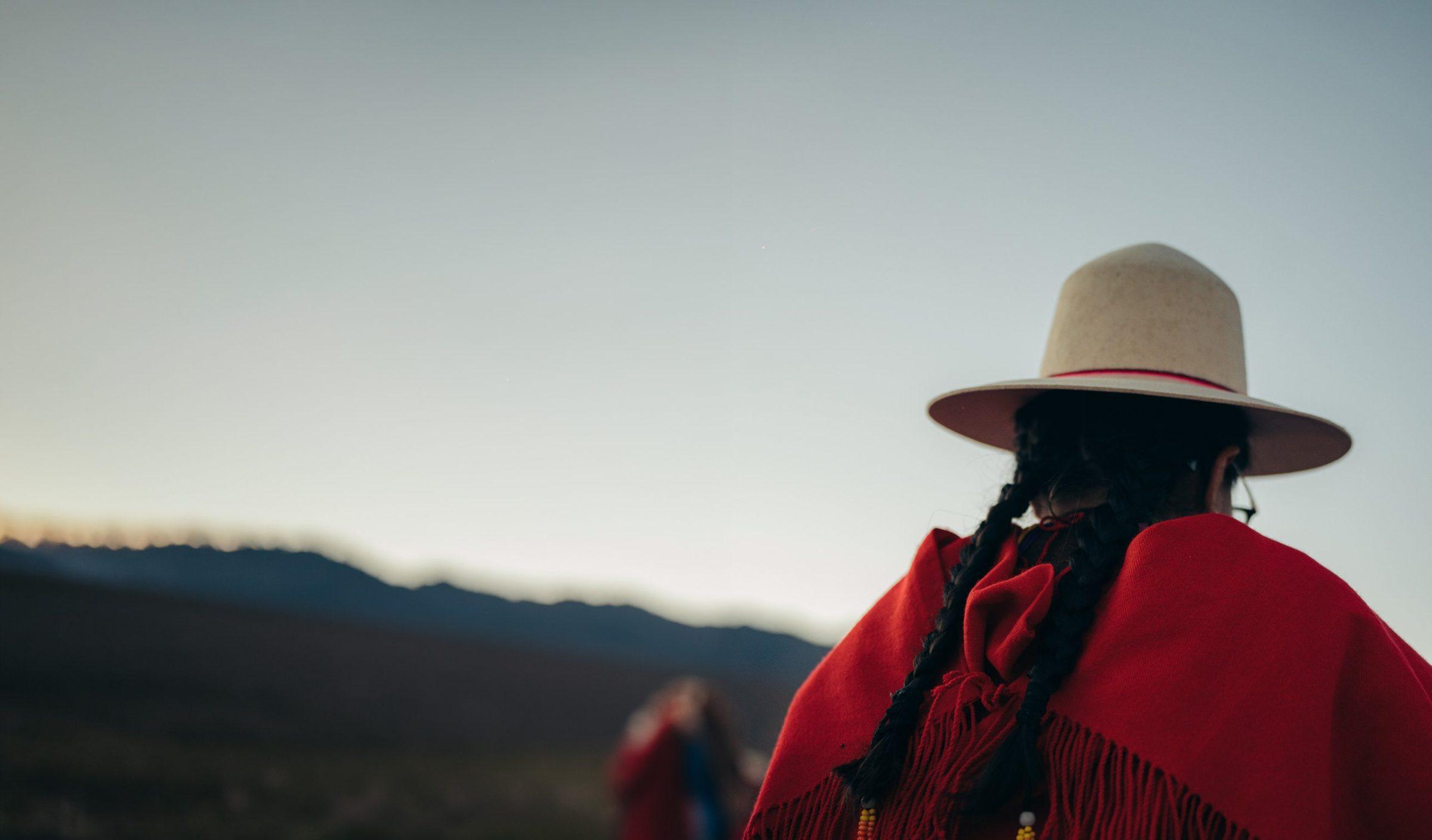Joven con sombrero y manta roja mirando el horizonte en el altiplano al atardecer